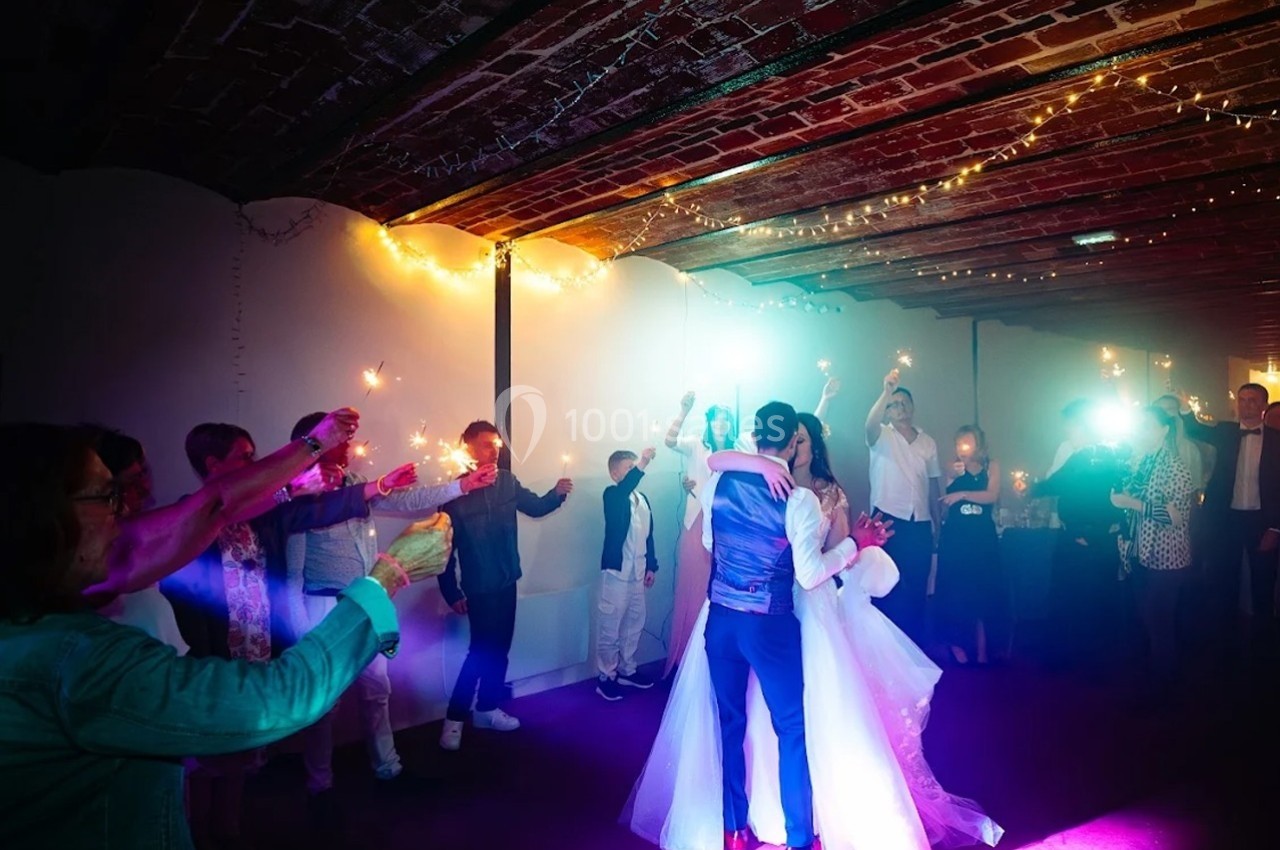 Un couple danse sous des lumières colorées, entouré d'invités tenant des cierges magiques dans une salle voûtée.