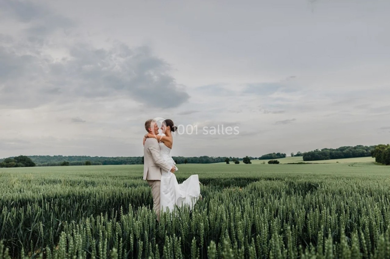 Un couple en tenue de mariage se tient dans un champ verdoyant sous un ciel nuageux.