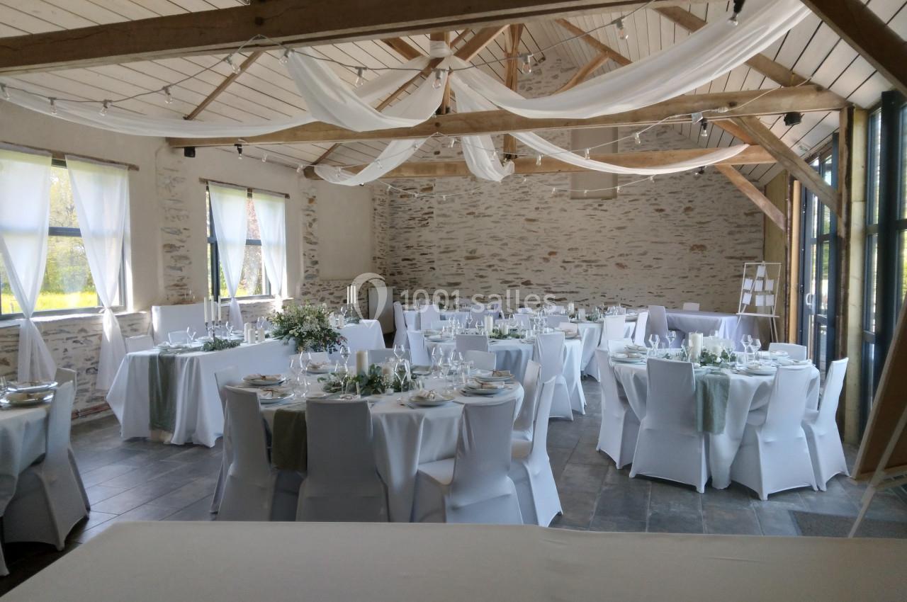 Salle de réception lumineuse avec tables rondes dressées, nappes blanches et décorations élégantes sous un plafond en bois.