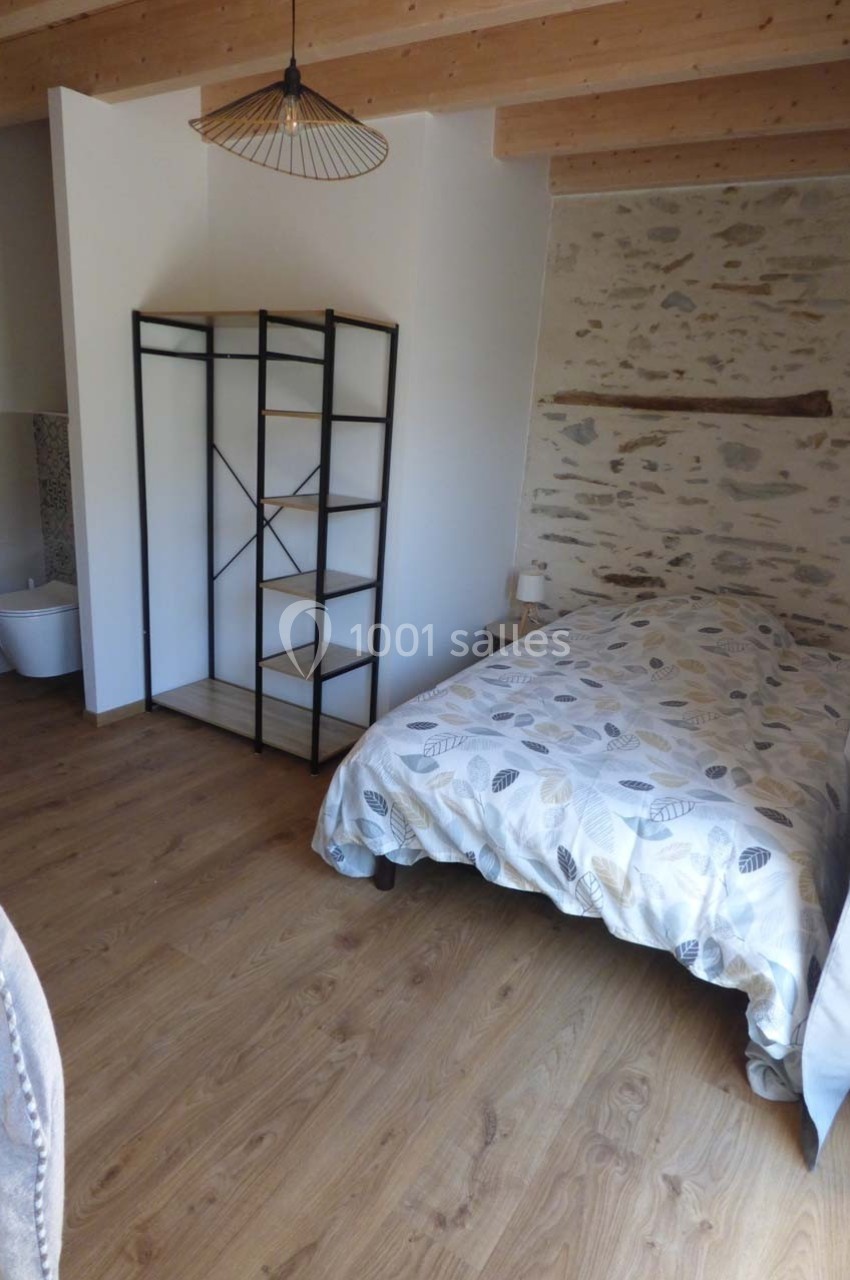 Chambre avec lit simple, étagère en métal, mur en pierre apparente et parquet en bois clair.