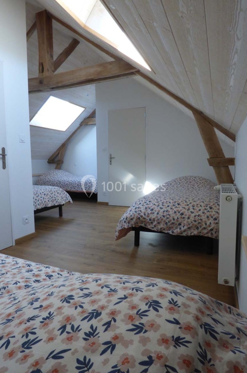 Chambre mansardée avec trois lits simples, parquet en bois clair, poutres apparentes et lumière naturelle.