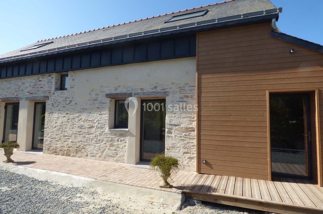 Façade d'une maison rénovée avec murs en pierre, bardage en bois et toit en ardoise, entourée d'une terrasse en bois.
