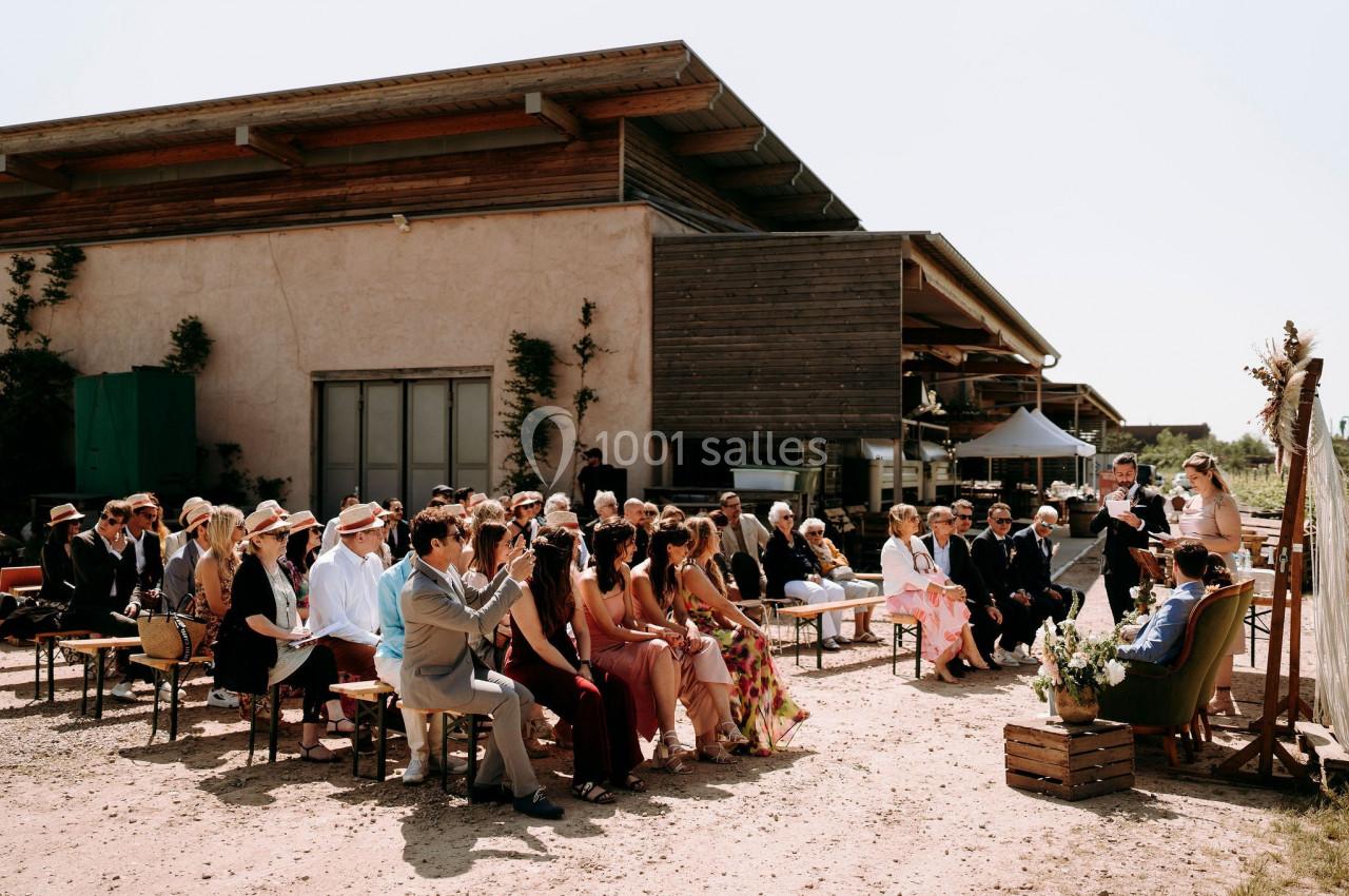 Cérémonie de mariage en plein air avec des invités assis face à un couple et un officiant devant une arche fleurie.