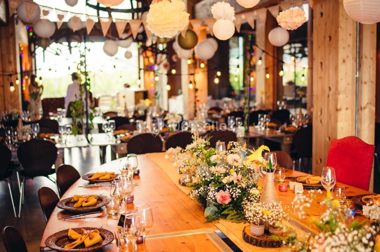 Salle de réception décorée avec des guirlandes lumineuses, des fleurs et des tables dressées pour un événement festif.