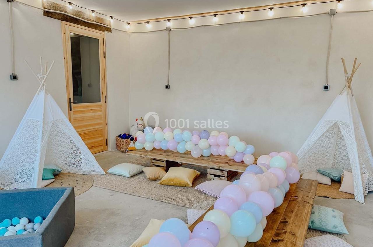 Deux tipis blancs décorent une pièce lumineuse avec des guirlandes, des ballons pastel et des coussins au sol.