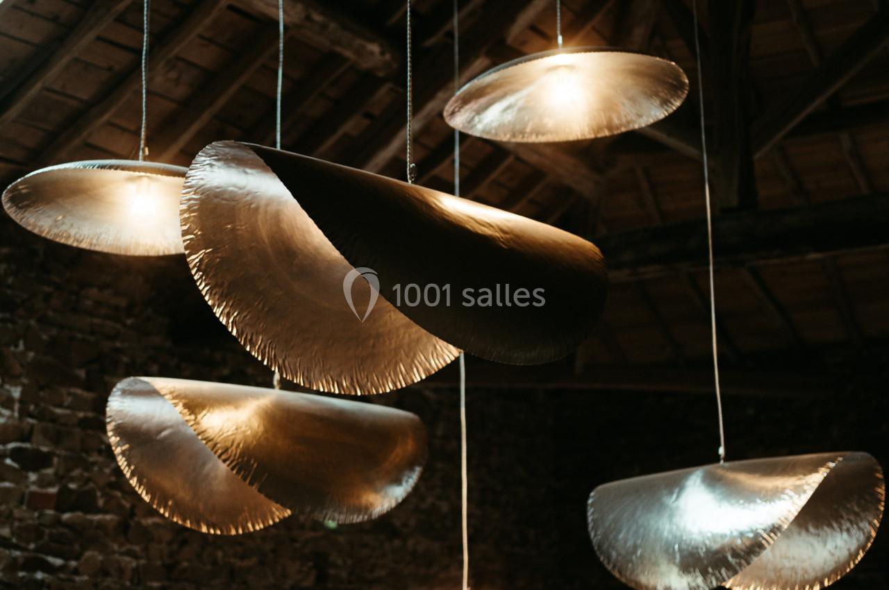 Suspensions lumineuses en métal aux formes organiques, accrochées sous un plafond en bois dans un espace en pierre.