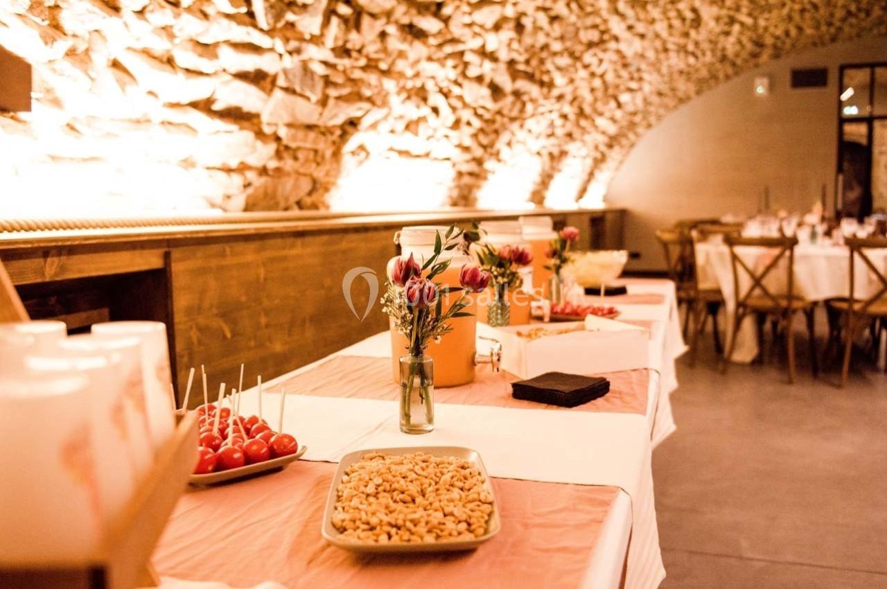 Table de buffet décorée avec des fleurs et des plats, dans une salle voûtée en pierre éclairée chaleureusement.