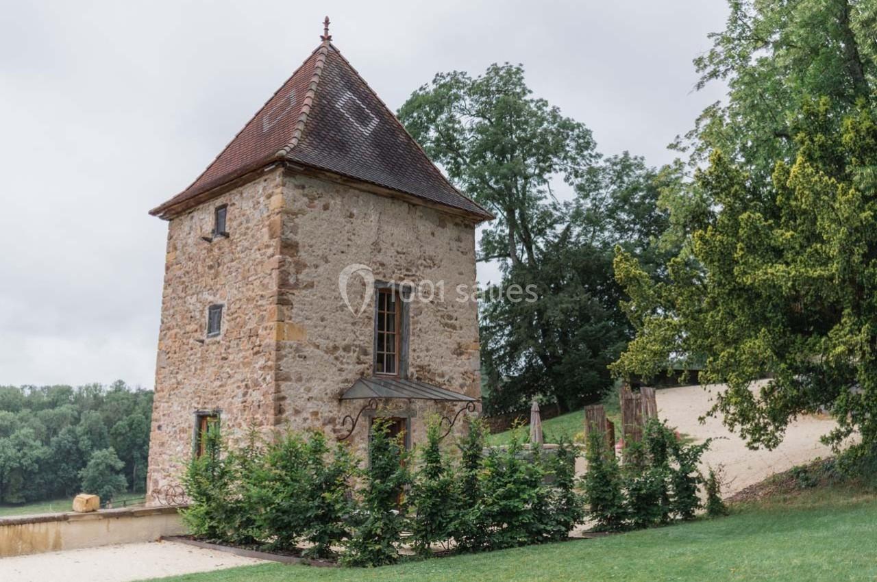Tour en pierre ancienne avec toit en tuiles, entourée de verdure et située dans un paysage rural.