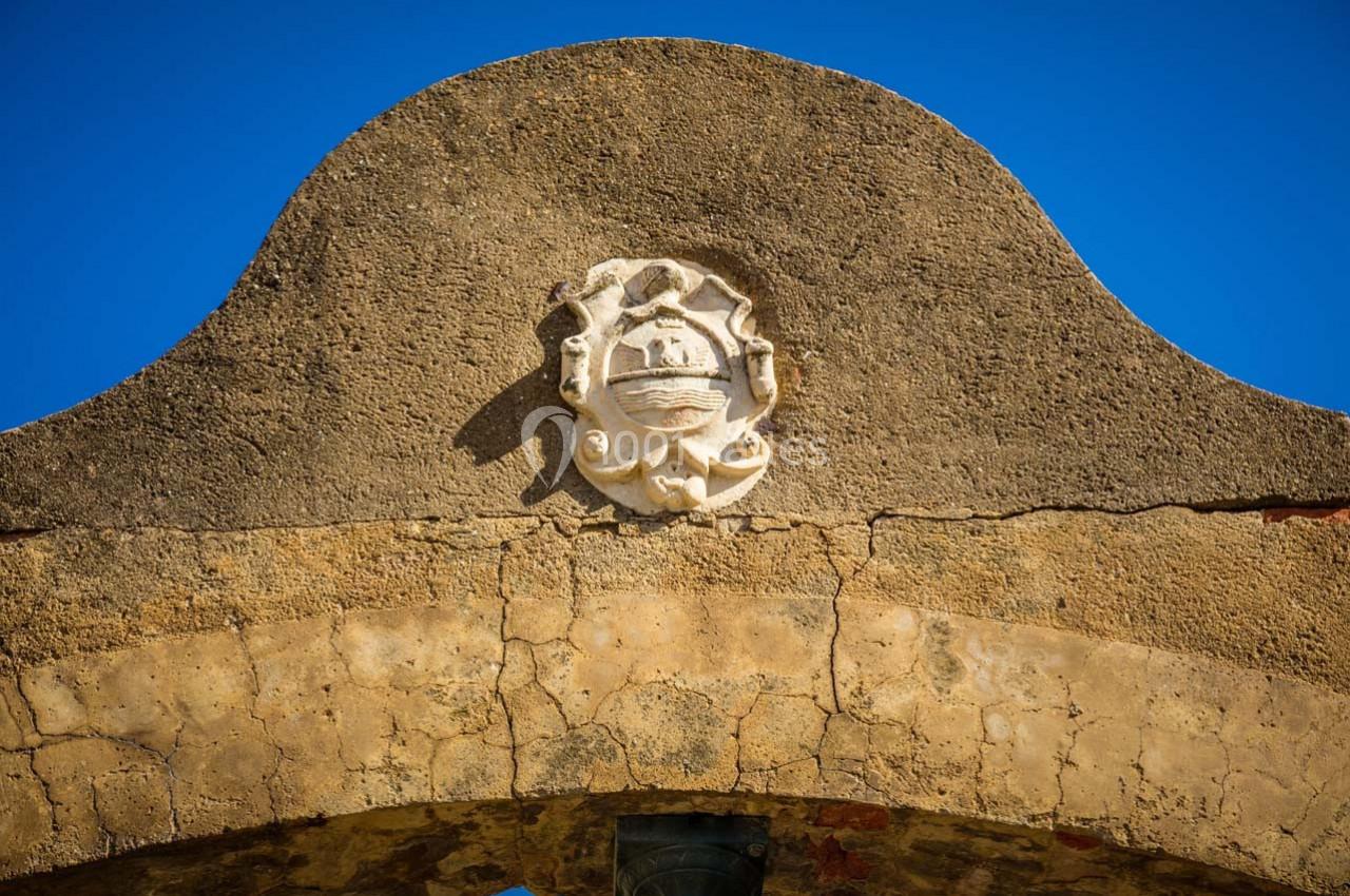 Détail d'un blason sculpté sur une arche en pierre ancienne, sous un ciel bleu clair.