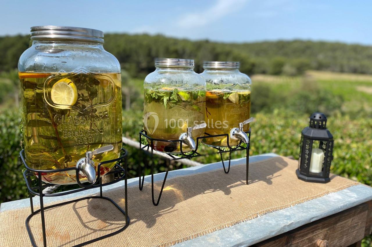Distributeurs en verre remplis de boissons infusées aux herbes et au citron, posés sur une table en extérieur.