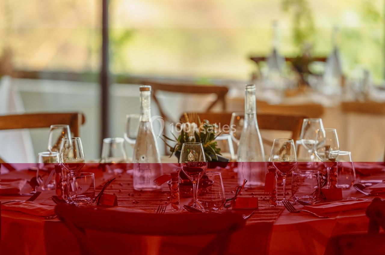 Table dressée avec nappes rouges, verres, bouteilles d'eau et décoration florale, dans un cadre lumineux.