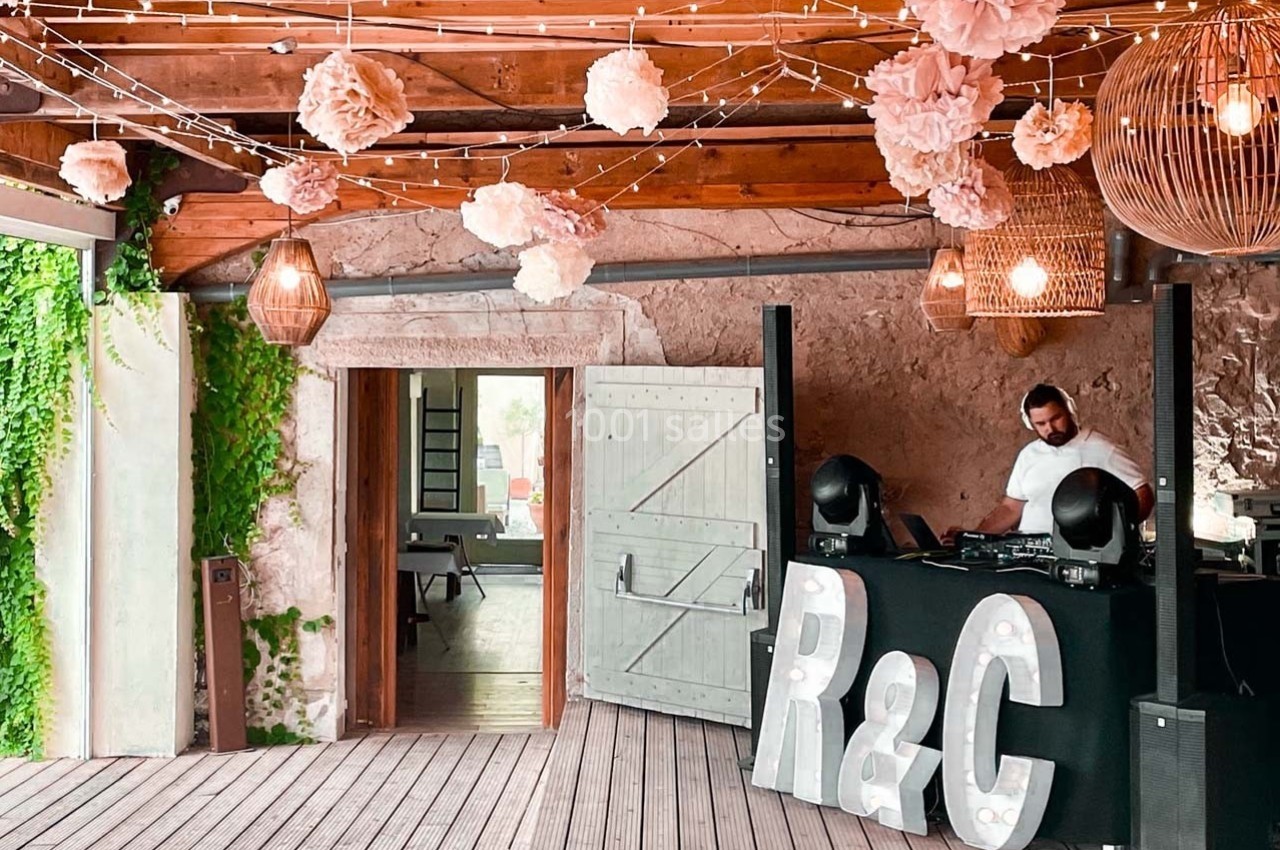 Salle décorée avec des guirlandes lumineuses et des fleurs suspendues, DJ en arrière-plan près des lettres ’R&C’.