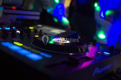Structure en bois d'une halle éclairée par des lumières violettes, avec un toit en tuiles et des piliers en pierre.