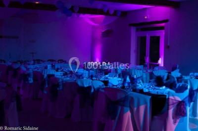 Structure en bois d'une halle éclairée par des lumières violettes, avec un toit en tuiles et des piliers en pierre.