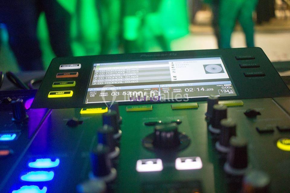 Table de mixage avec écran affichant des pistes audio, entourée de boutons lumineux dans un environnement sombre.