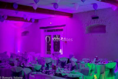 Structure en bois d'une halle éclairée par des lumières violettes, avec un toit en tuiles et des piliers en pierre.