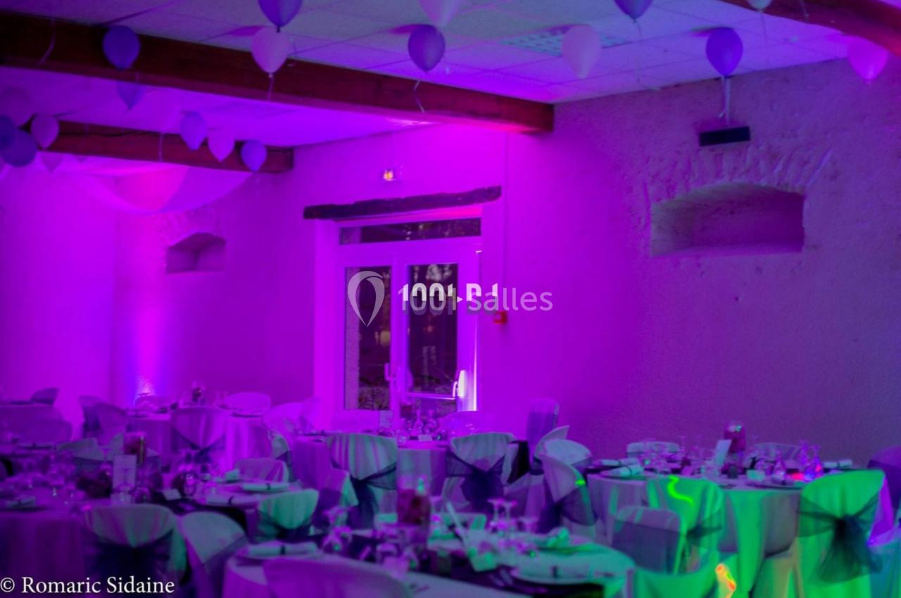 Salle de réception décorée avec des tables dressées, des ballons suspendus et un éclairage violet.