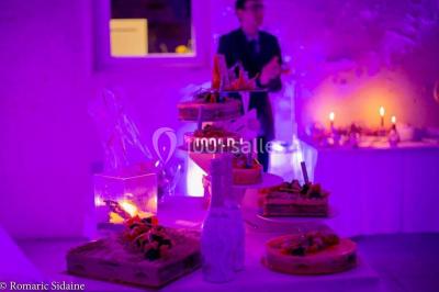 Structure en bois d'une halle éclairée par des lumières violettes, avec un toit en tuiles et des piliers en pierre.