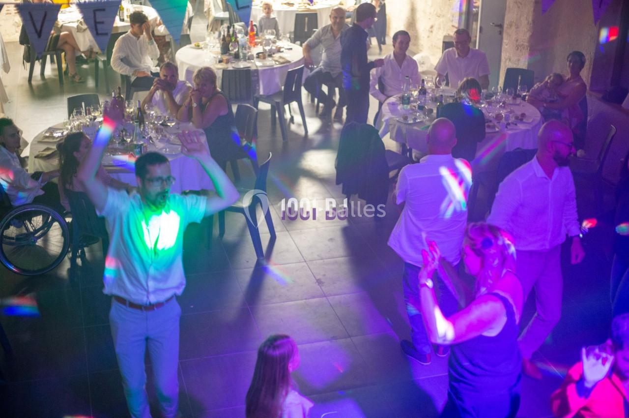 Des personnes dansent et discutent autour de tables lors d'une soirée festive avec éclairages colorés.