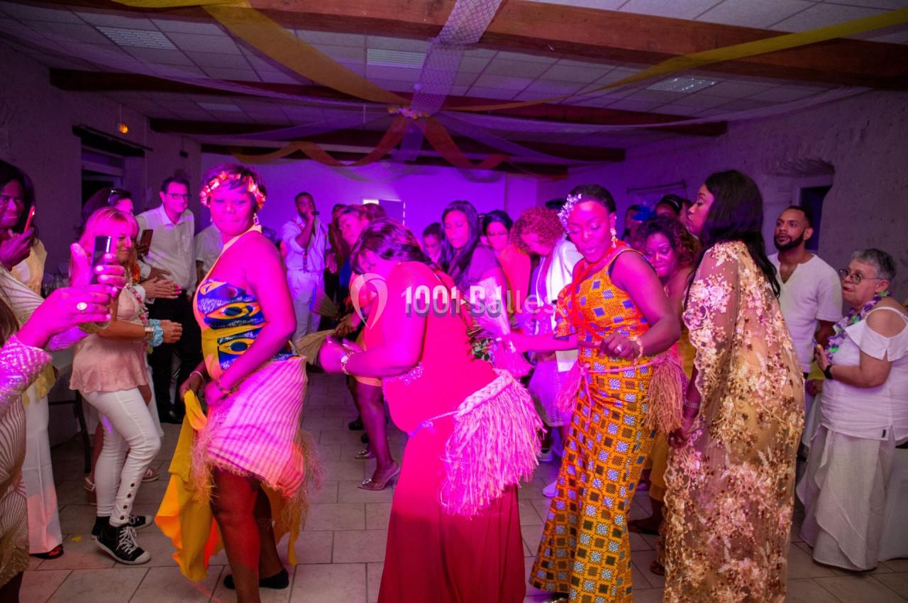 Des personnes dansent lors d'une fête dans une salle décorée avec des guirlandes et un éclairage coloré.