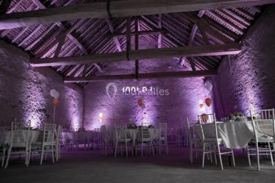 Structure en bois d'une halle éclairée par des lumières violettes, avec un toit en tuiles et des piliers en pierre.