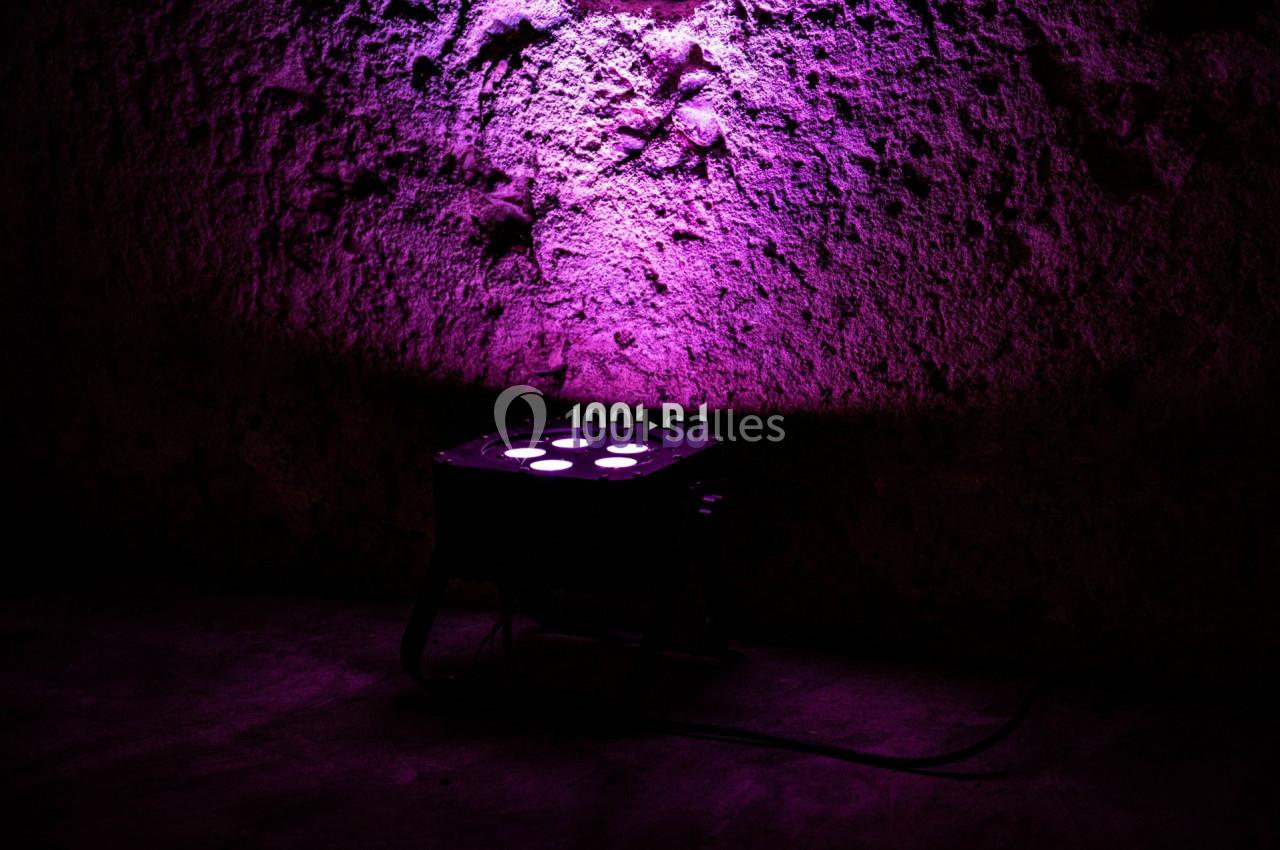 Projecteur lumineux diffusant une lumière violette sur un mur texturé dans un environnement sombre.