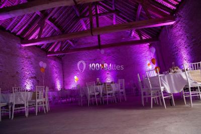Structure en bois d'une halle éclairée par des lumières violettes, avec un toit en tuiles et des piliers en pierre.