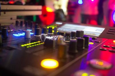 Structure en bois d'une halle éclairée par des lumières violettes, avec un toit en tuiles et des piliers en pierre.