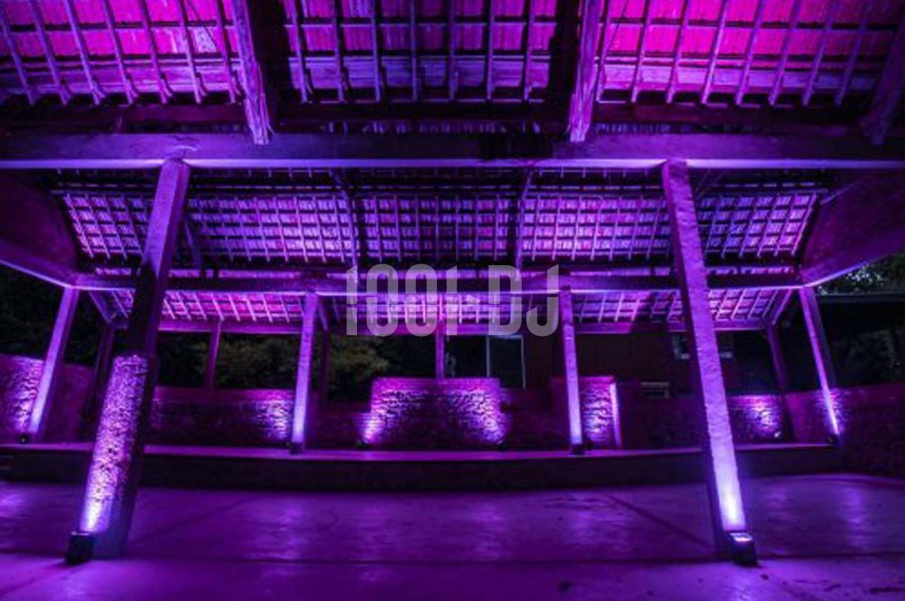 Structure en bois d'une halle éclairée par des lumières violettes, avec un toit en tuiles et des piliers en pierre.
