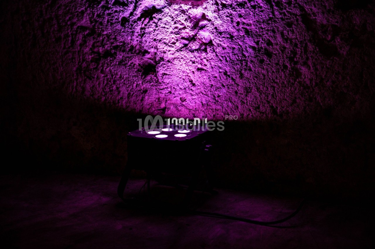 Projecteur lumineux diffusant une lumière violette sur un mur texturé dans un environnement sombre.