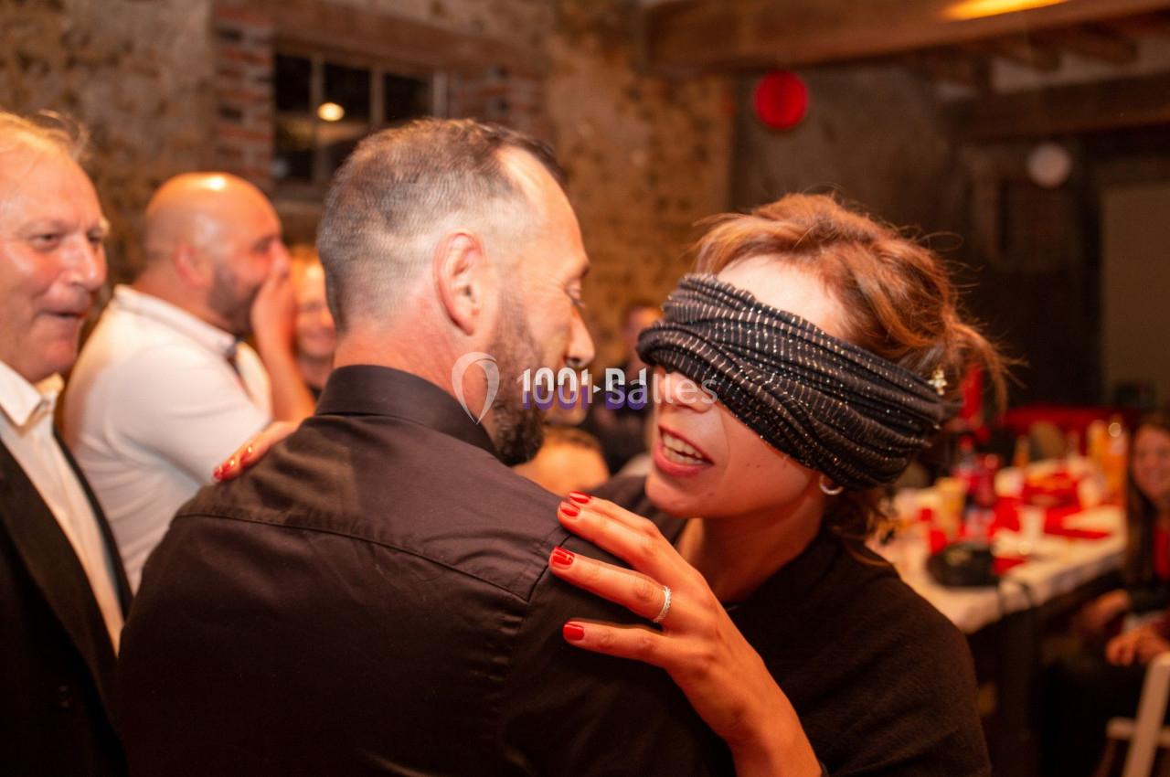 Une femme aux yeux bandés sourit en touchant un homme dans une ambiance festive et conviviale.
