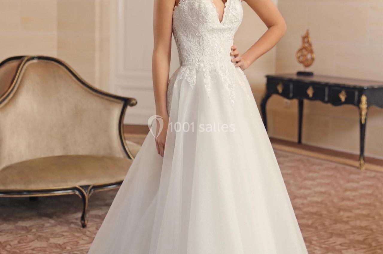 Femme portant une robe de mariée blanche avec un haut en dentelle, posant dans une pièce élégante au décor classique.