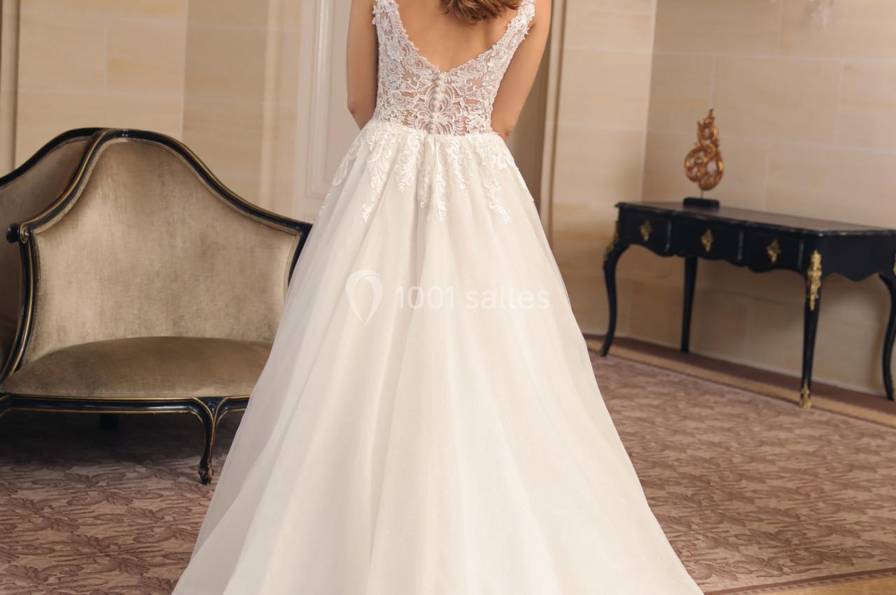 Femme de dos portant une robe de mariée avec un corsage en dentelle, dans une pièce élégante avec mobilier classique.