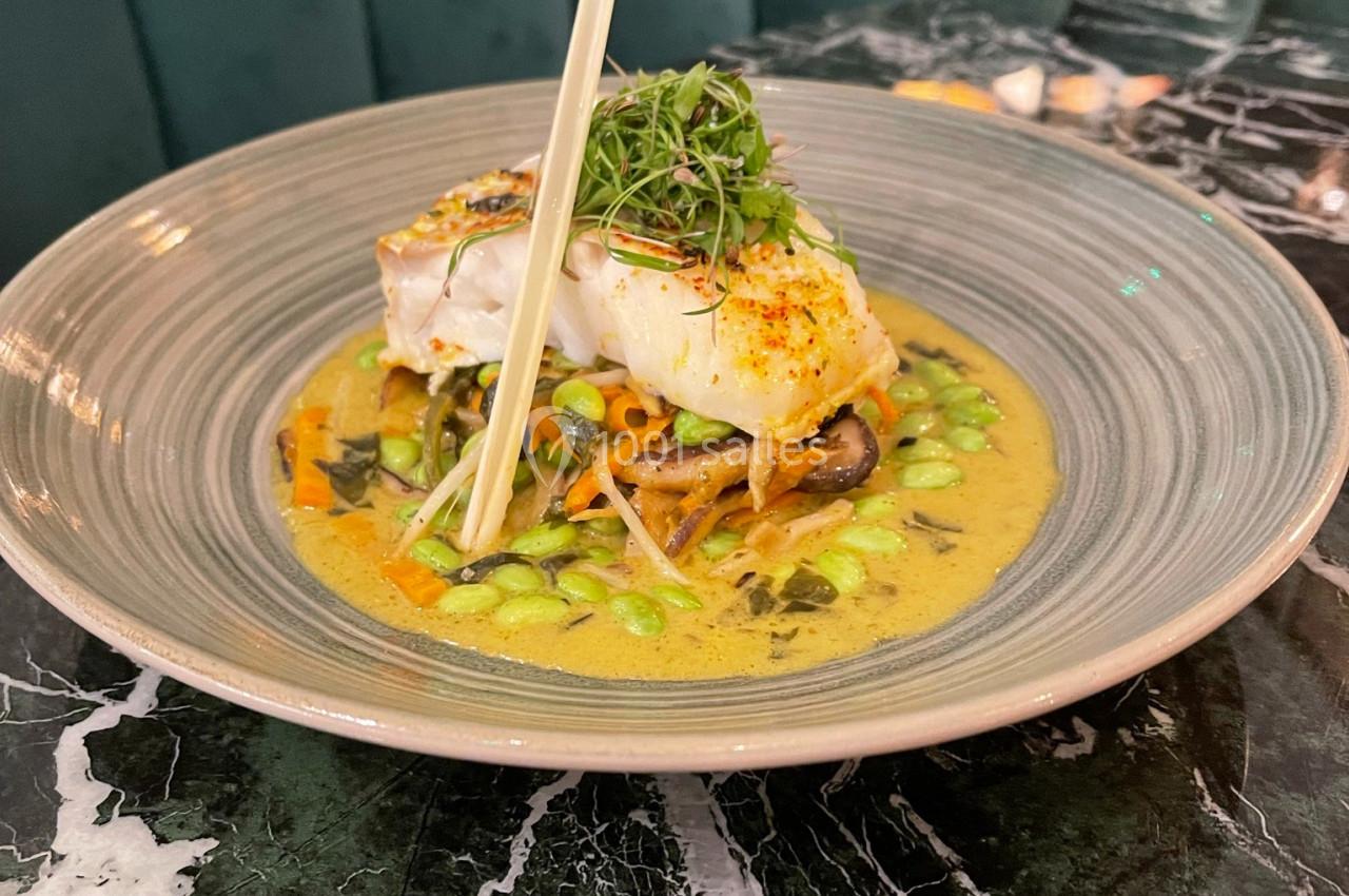 Plat de poisson blanc sur un lit de légumes et nouilles dans une sauce crémeuse, servi dans une assiette sur une table en…