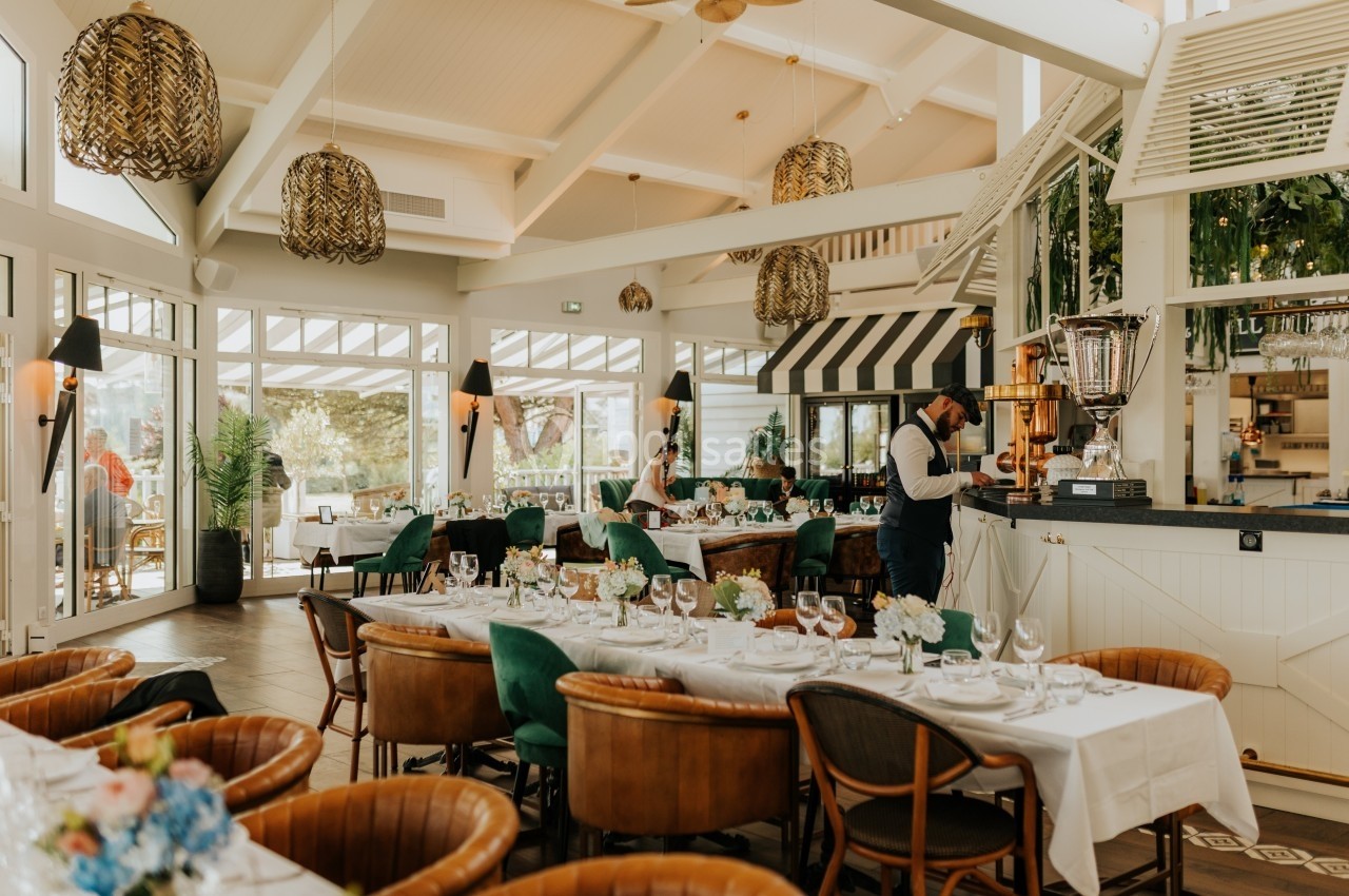 Salle de restaurant lumineuse avec tables dressées, chaises en cuir et décoration élégante sous un plafond haut.