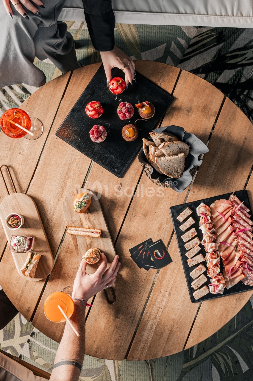Vue de dessus d'une table en bois avec des planches apéritives, tapas variés et boissons colorées.