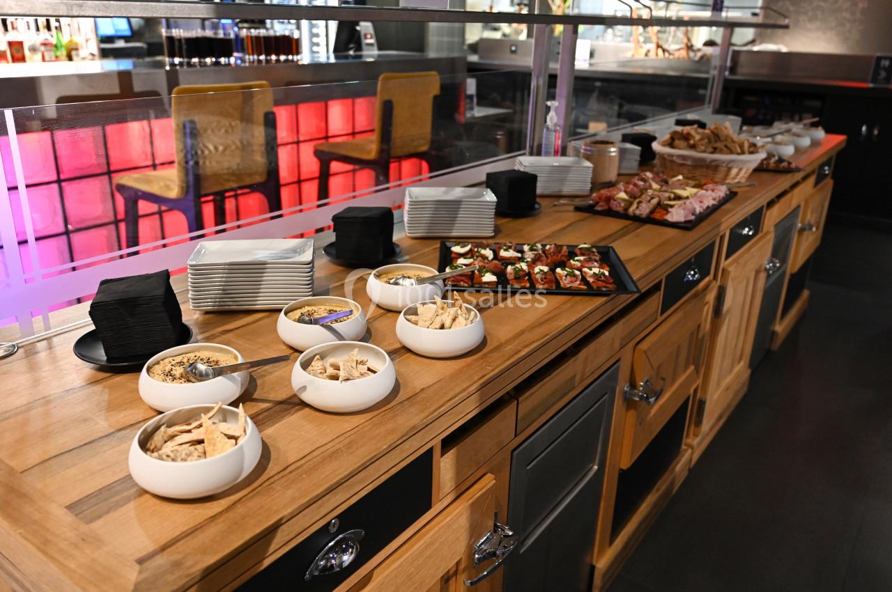 Buffet avec assiettes, bols de snacks, toasts garnis et viennoiseries sur un comptoir en bois dans un espace moderne.
