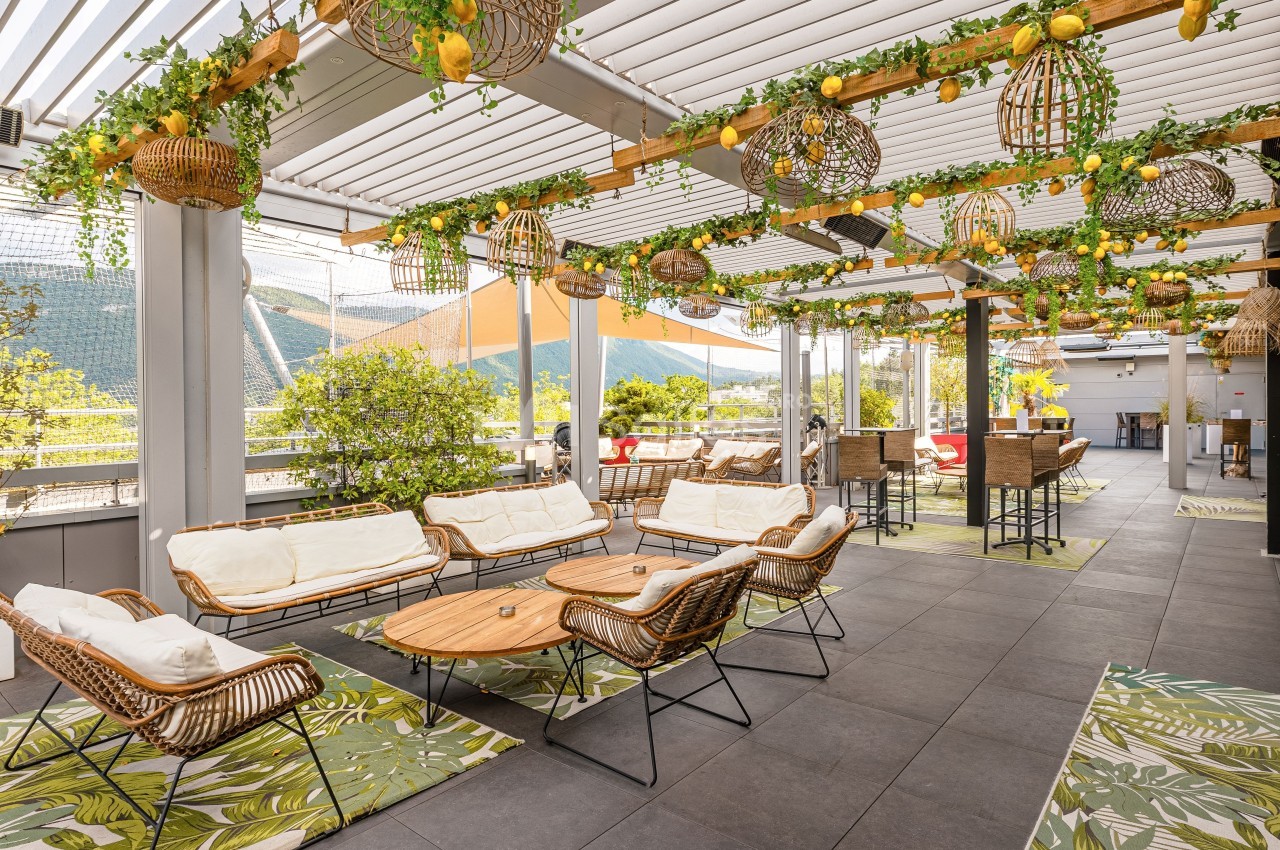 Terrasse aménagée avec mobilier en rotin, plantes suspendues et vue sur un paysage montagneux en arrière-plan.