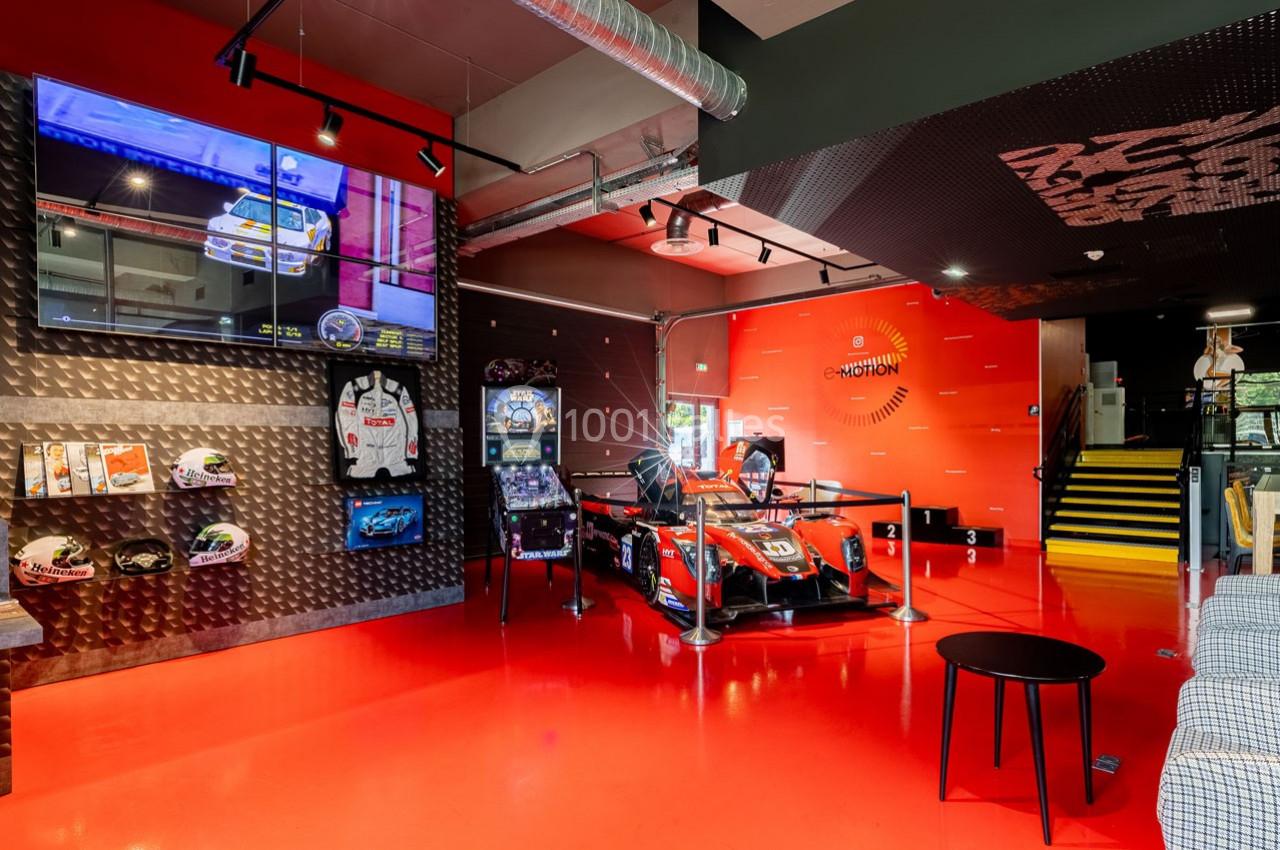 Salle avec simulateur de course, écran géant, équipements de sport automobile exposés et sol rouge brillant.