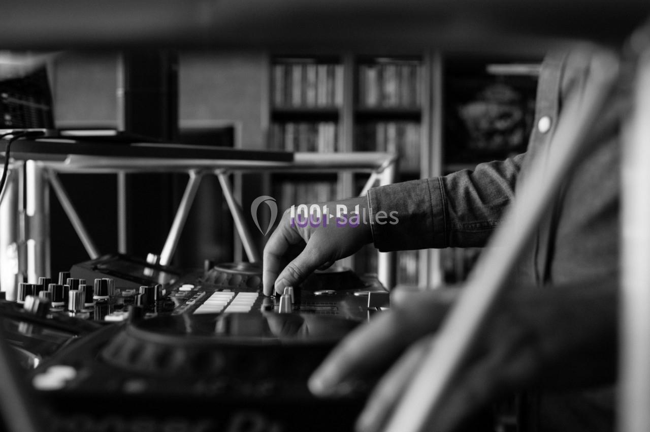 Un DJ ajuste les commandes d'une table de mixage dans un environnement intérieur, en noir et blanc.