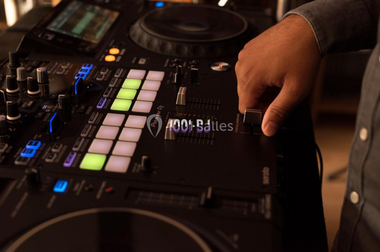 Main d'une personne ajustant un curseur sur une console de mixage DJ avec des boutons et lumières colorées.