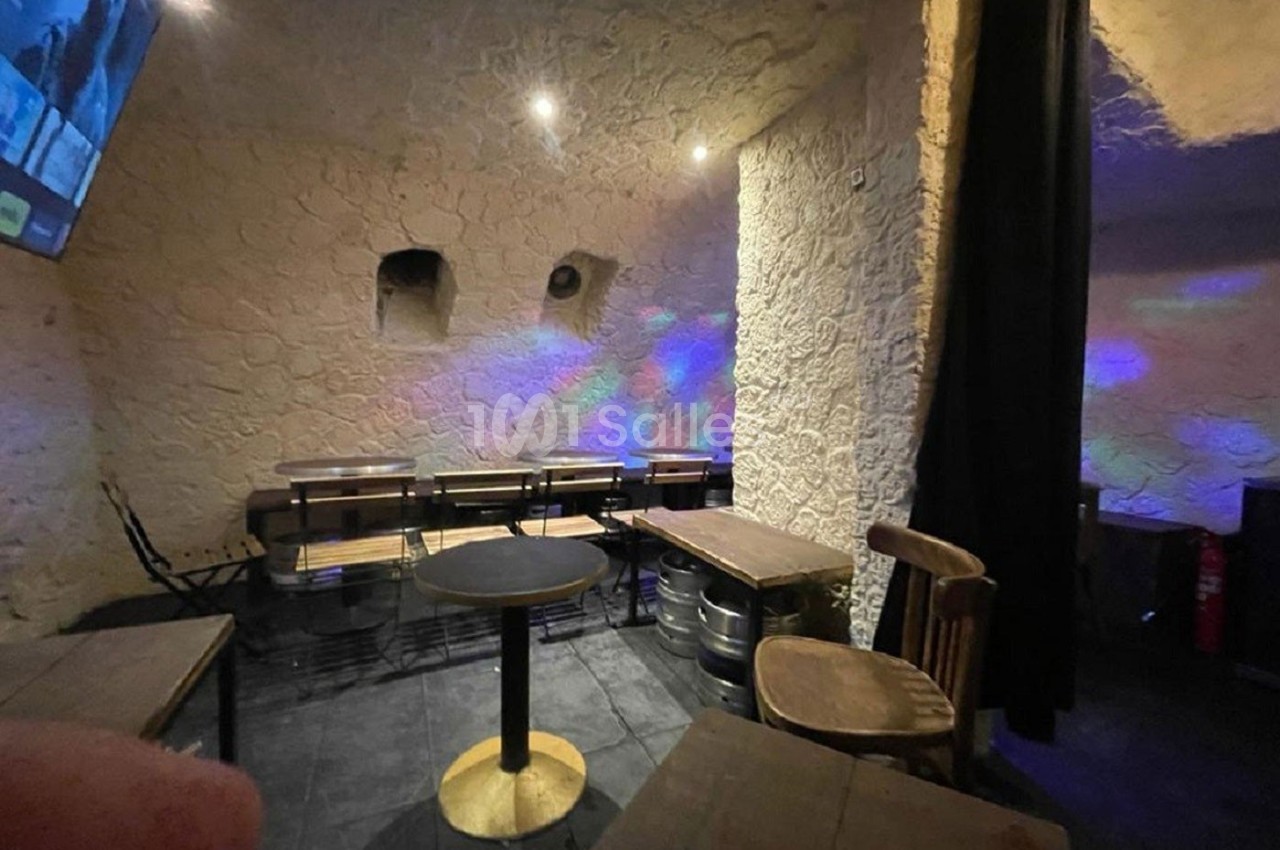 Salle avec murs en pierre, tables en bois, chaises simples et éclairage tamisé avec reflets colorés.