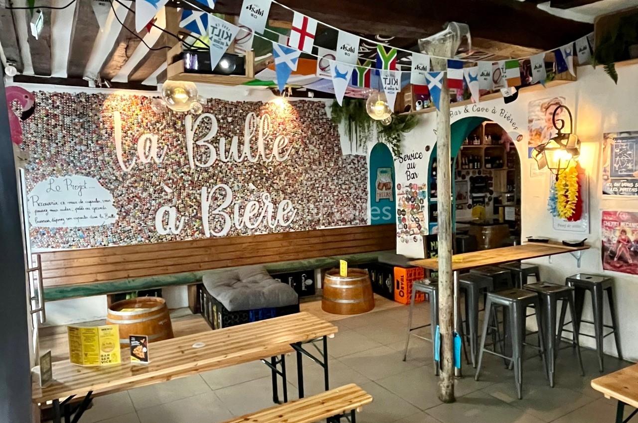 Intérieur d'un bar avec des tables en bois, des drapeaux suspendus et une décoration murale colorée.