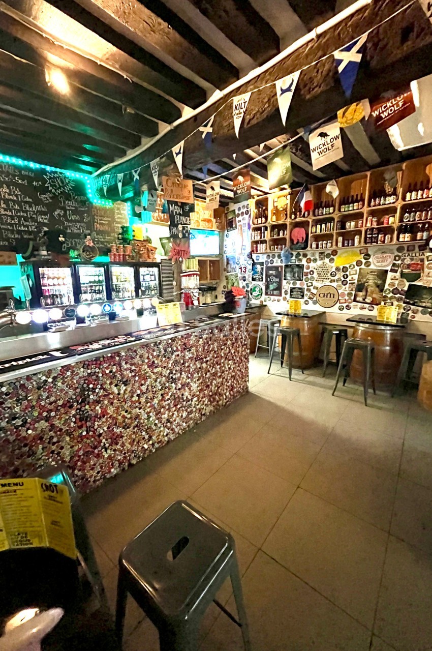 Intérieur d'un bar décoré avec des drapeaux, des autocollants et des étagères remplies de bouteilles, avec un comptoir…