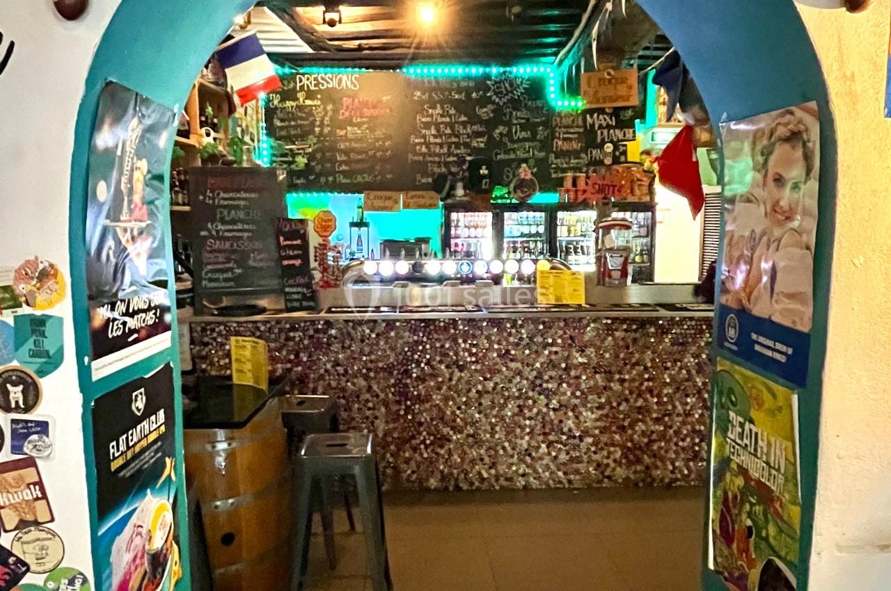 Entrée voûtée menant à un bar décoré avec des affiches, des lumières colorées et un comptoir en mosaïque.