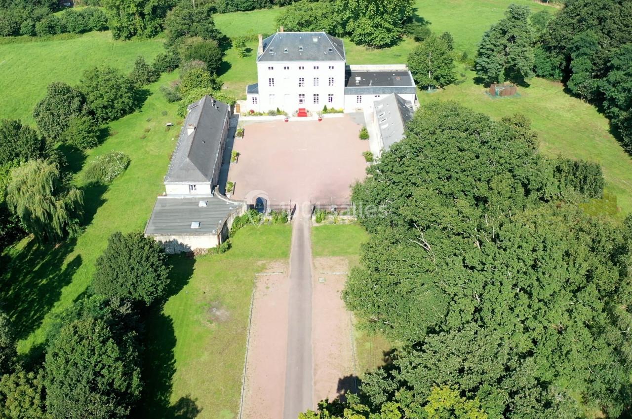 Vue aérienne d'un domaine avec une grande maison principale, des bâtiments annexes et un espace vert environnant.