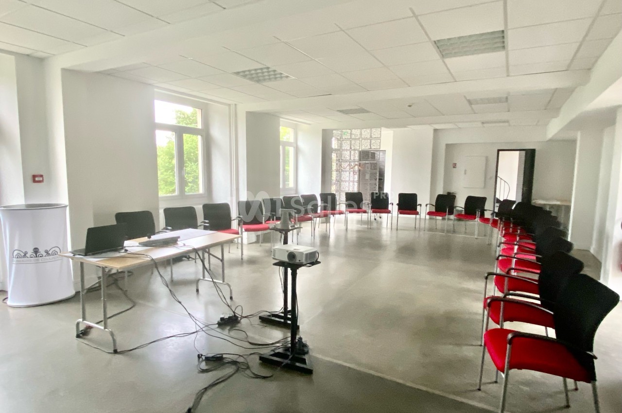 Salle de réunion lumineuse avec des chaises disposées en cercle, un projecteur et une table équipée d'un ordinateur.