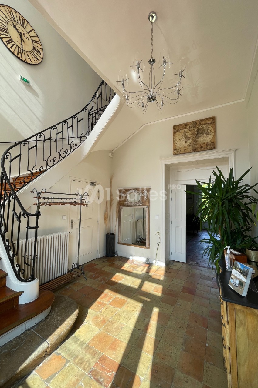 Entrée lumineuse avec escalier en bois, rampe en fer forgé, carrelage ancien et décoration murale.