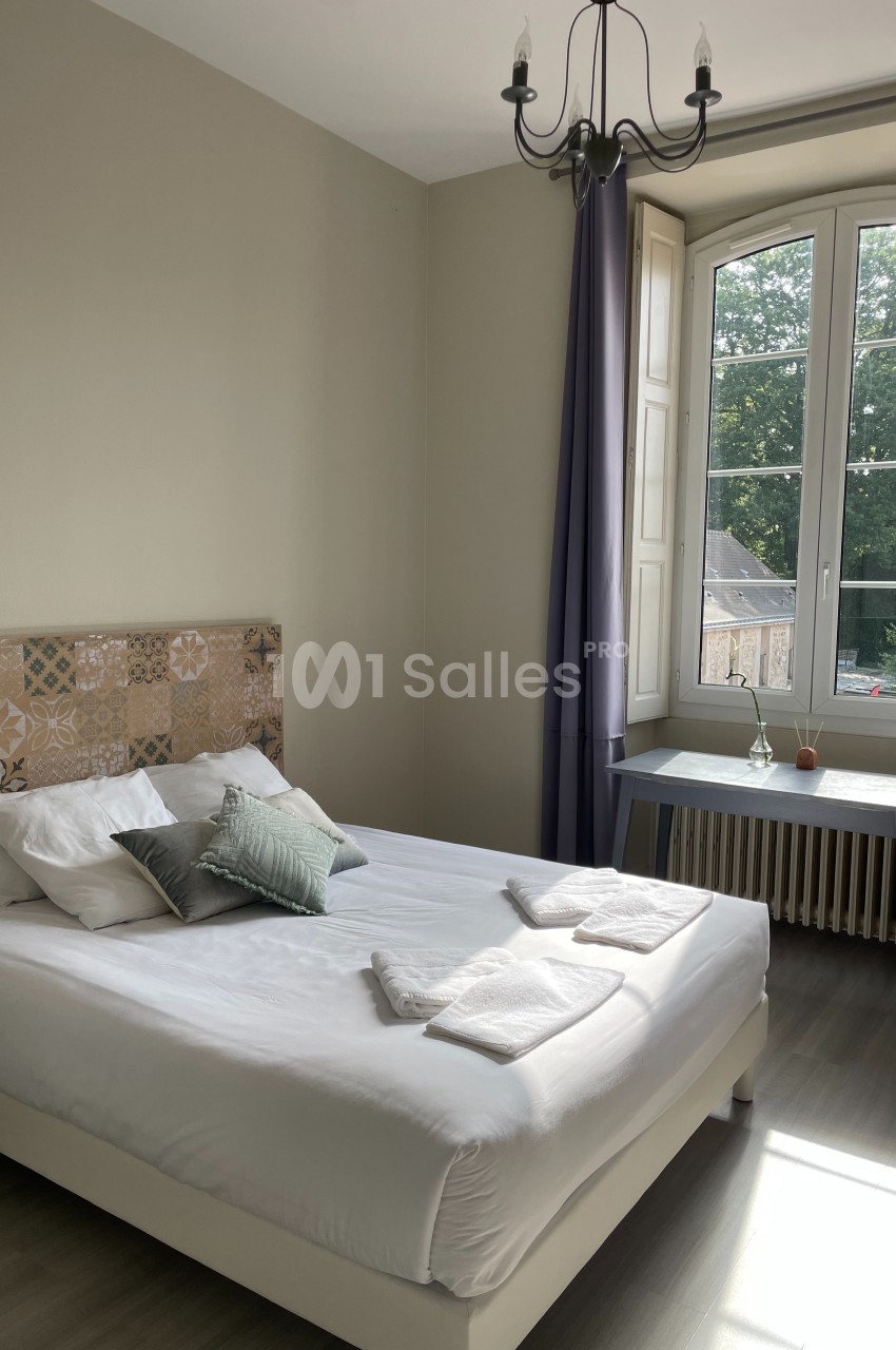 Chambre lumineuse avec lit double, tête de lit décorative, bureau près d'une fenêtre donnant sur un espace vert.