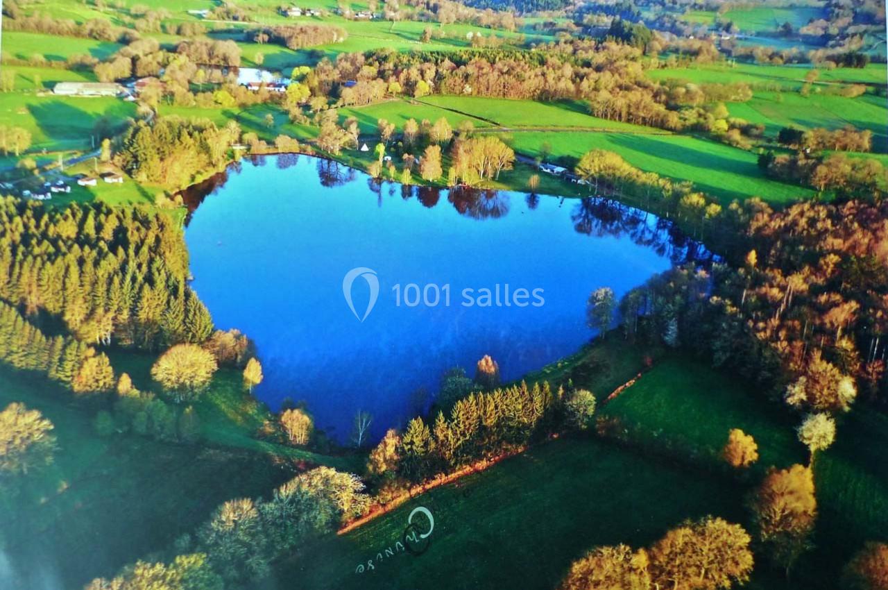 Vue aérienne d'un lac entouré de prairies, de forêts et de quelques habitations rurales dans un paysage verdoyant.